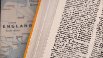 A dictionary is open to a page where the words "poise" and "poison" can be seen.