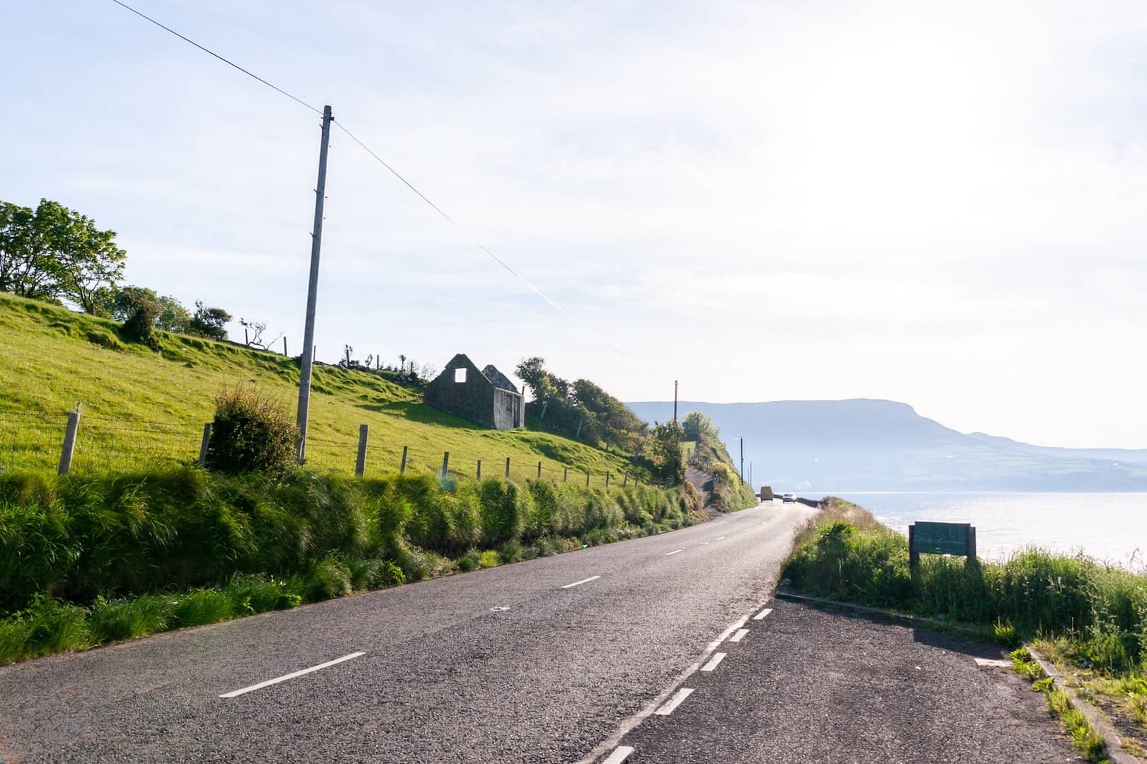 A road with a grassy hill on one side and water on the other.