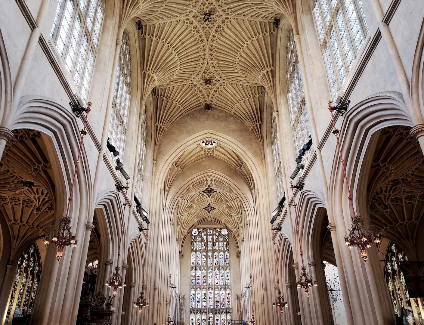 A cathedral with white walls, a vaulted ceiling, stained glass, and arches down the aisle.
