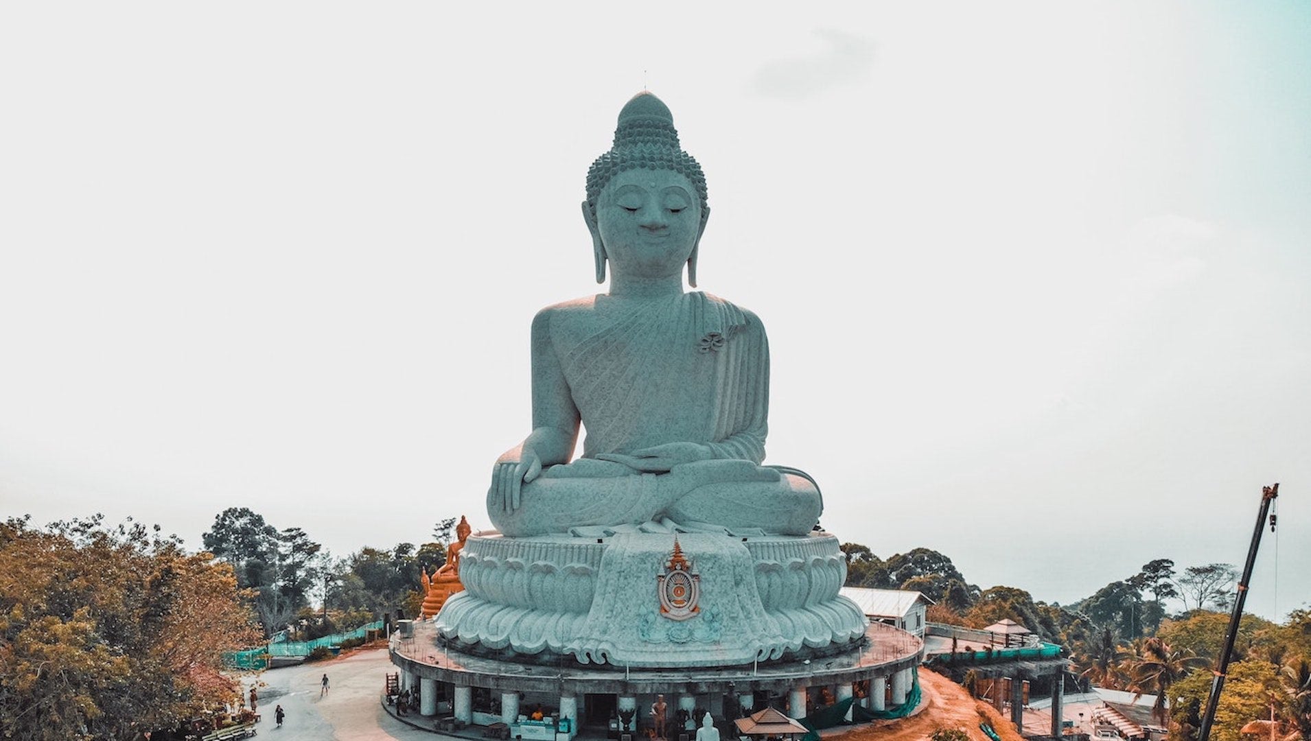 A large gray concrete statue of Buddha with people around it.