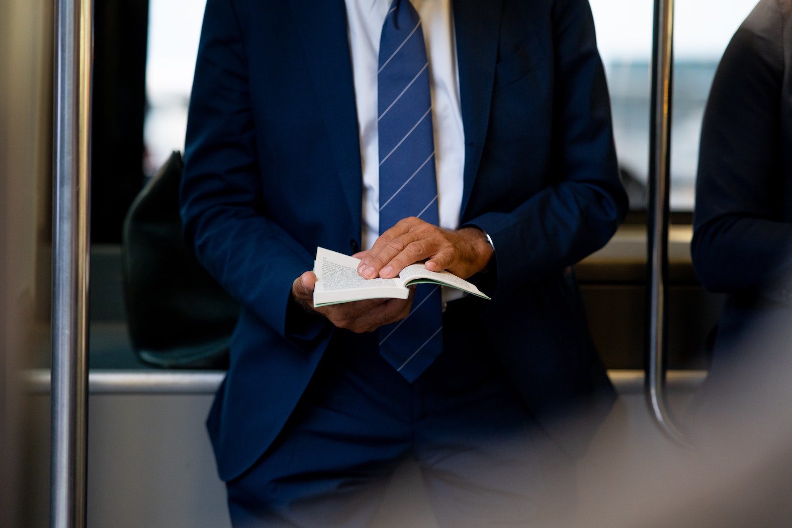 A man in a blue suit reading a book on a train.