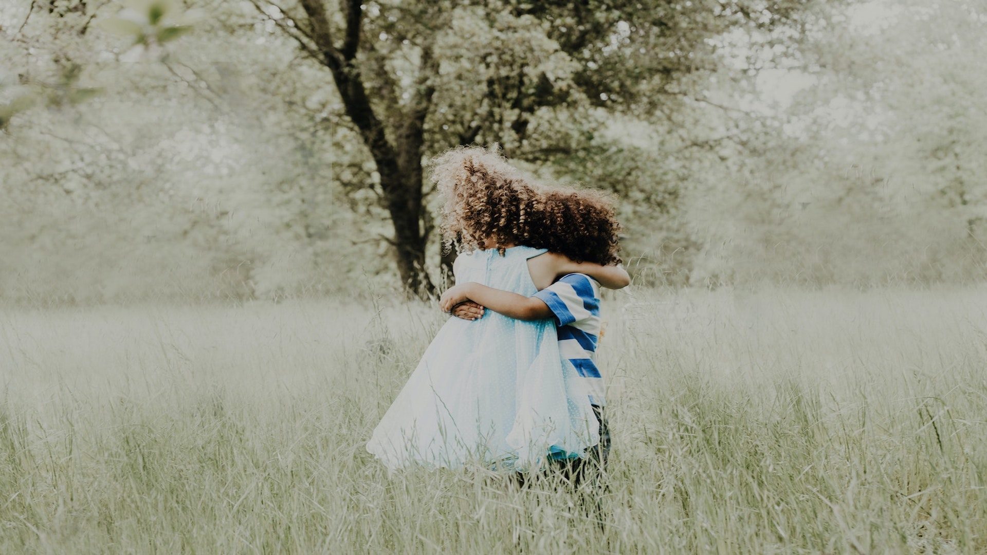 A young boy and girl hugging in a grassy field.