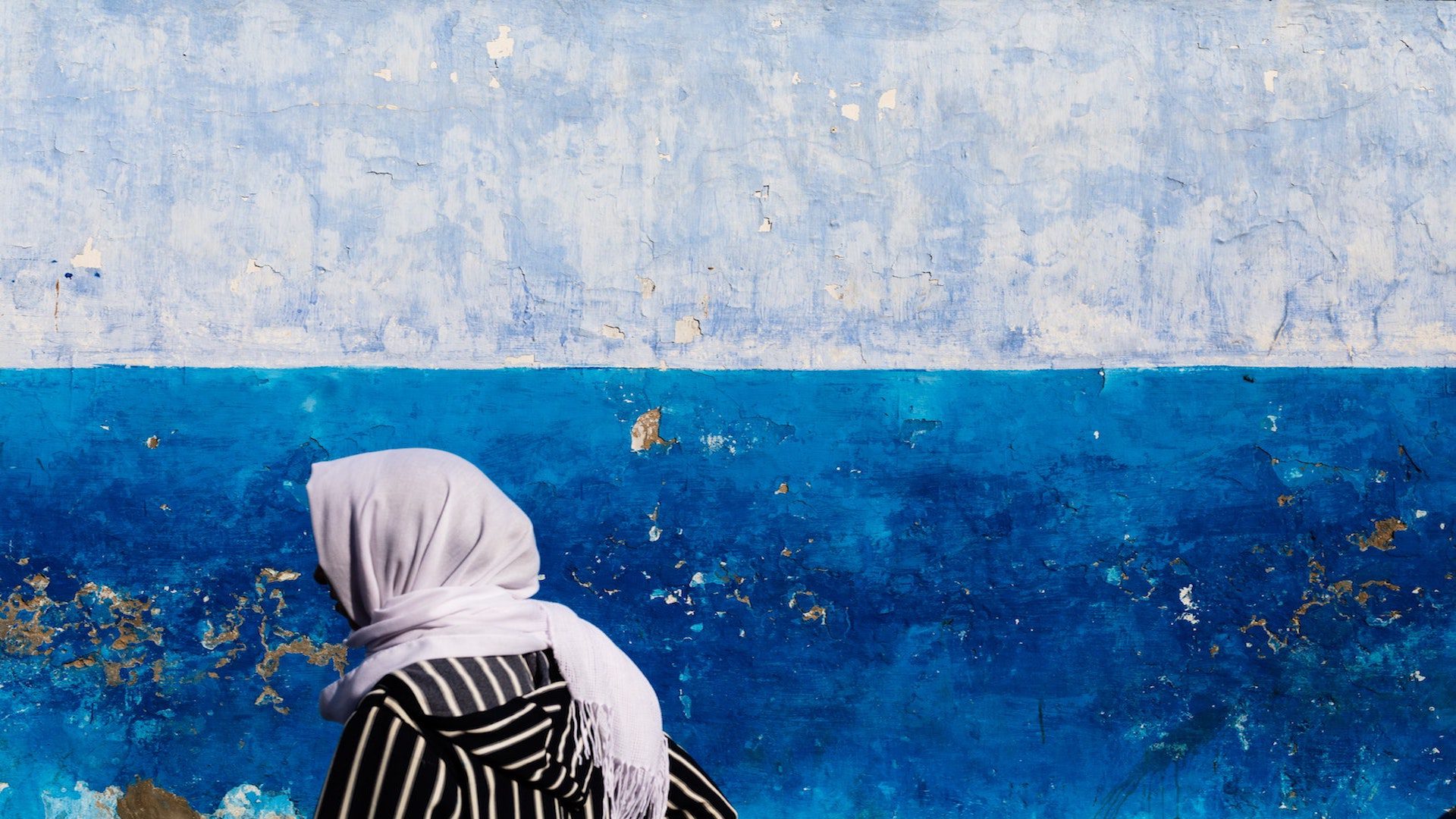 A woman wearing a hijab walking in front of a blue wall.