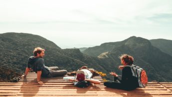 Three people sitting down overlooking mountains.