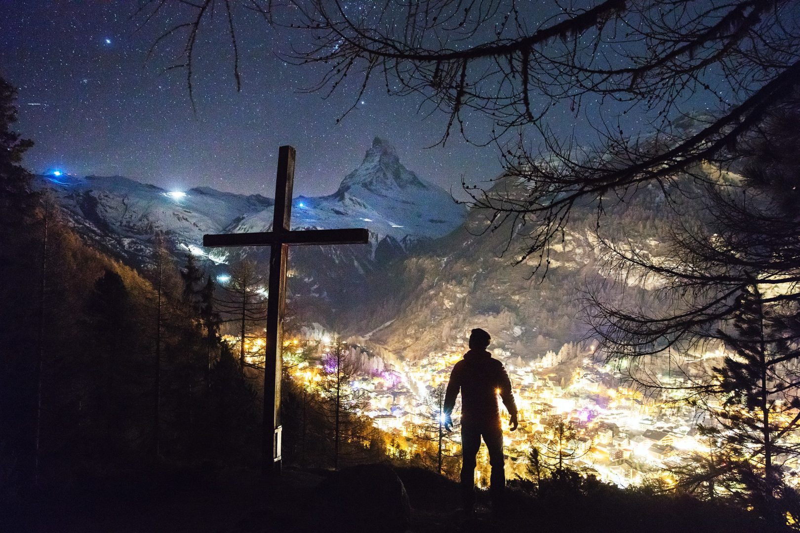 A picture of a man standing near a cross overlooking the night sky.