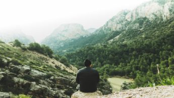 A man sitting on a rock on a mountain looking down over a forest.