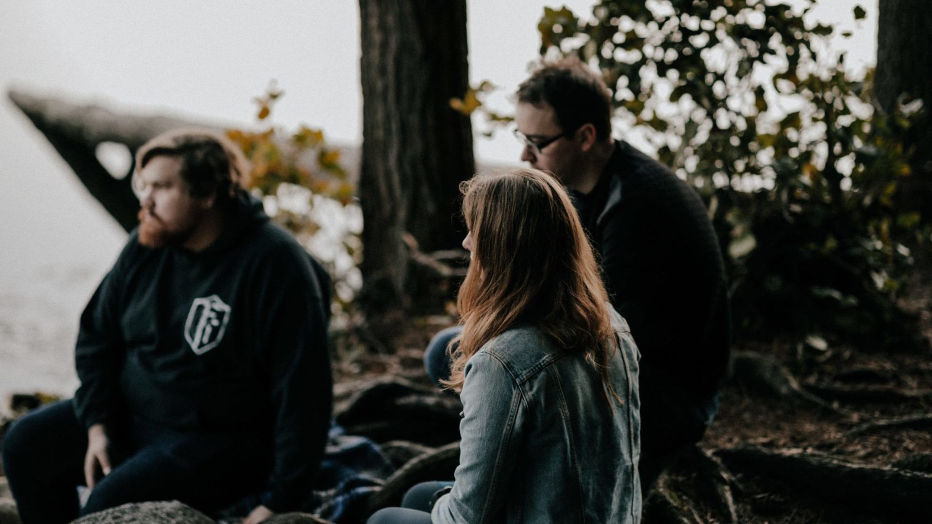 Two men and a women sitting on rocks near a river.