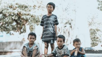 A group of four impoverished boys are sitting on the concrete together.