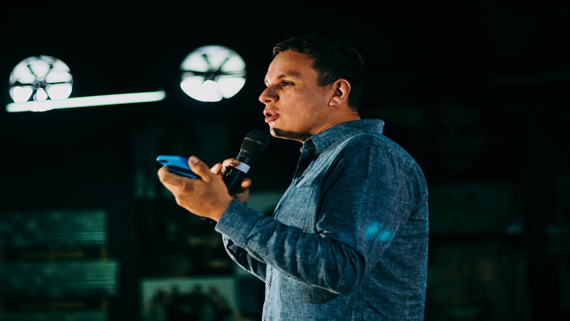 A pastor holding a microphone and his phone during a sermon.