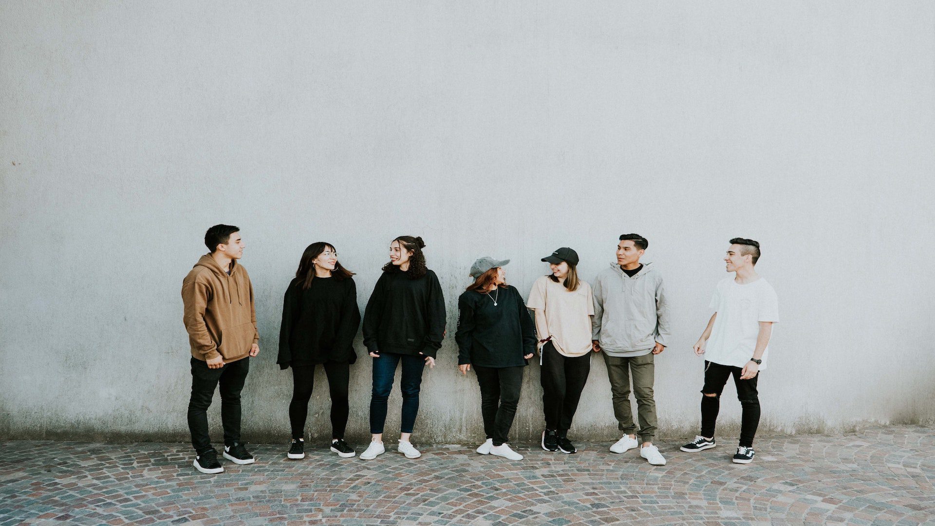 A group of young adults standing outside near a white wall.