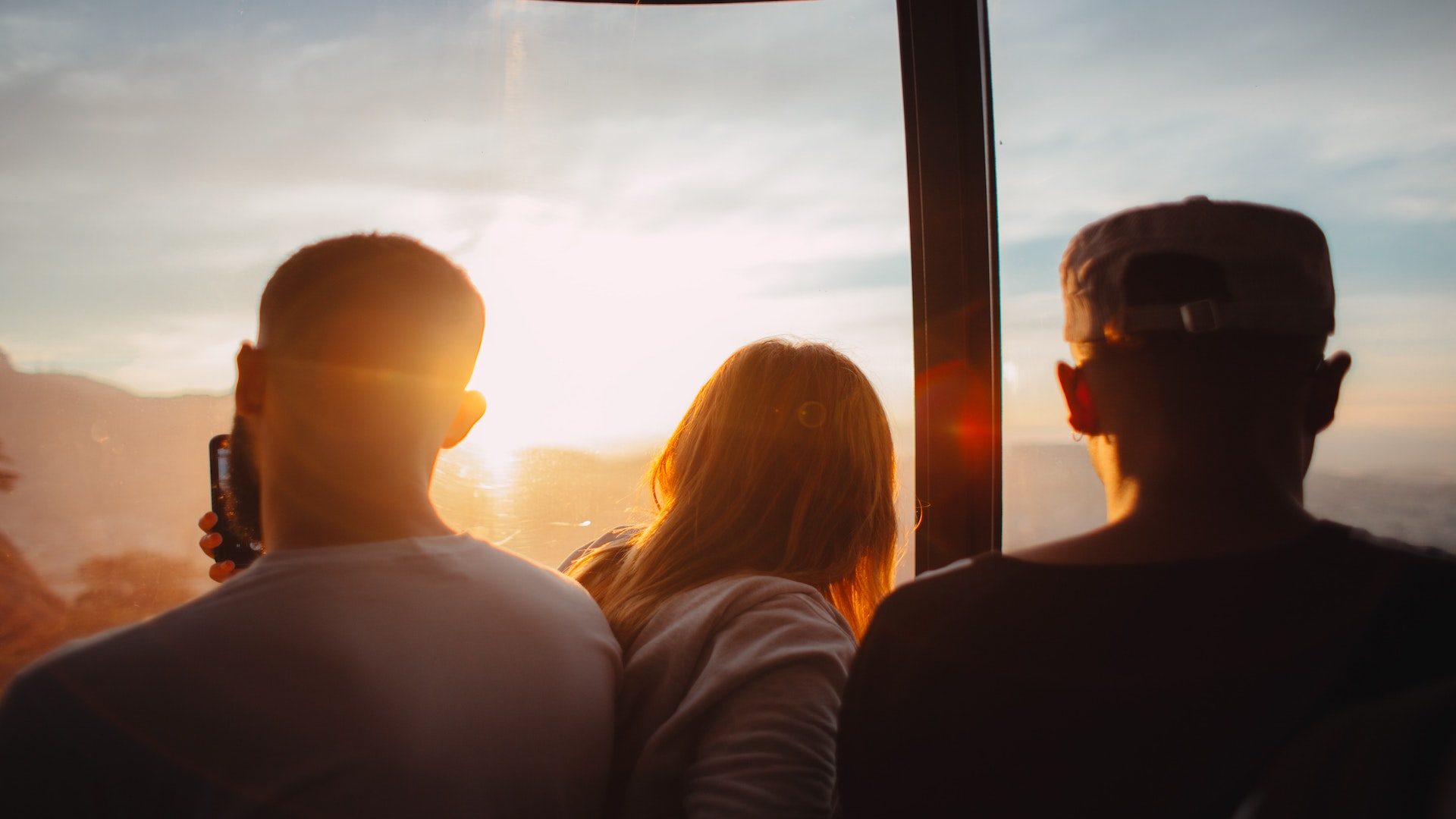 Two men and a woman looking out a window during sunset.