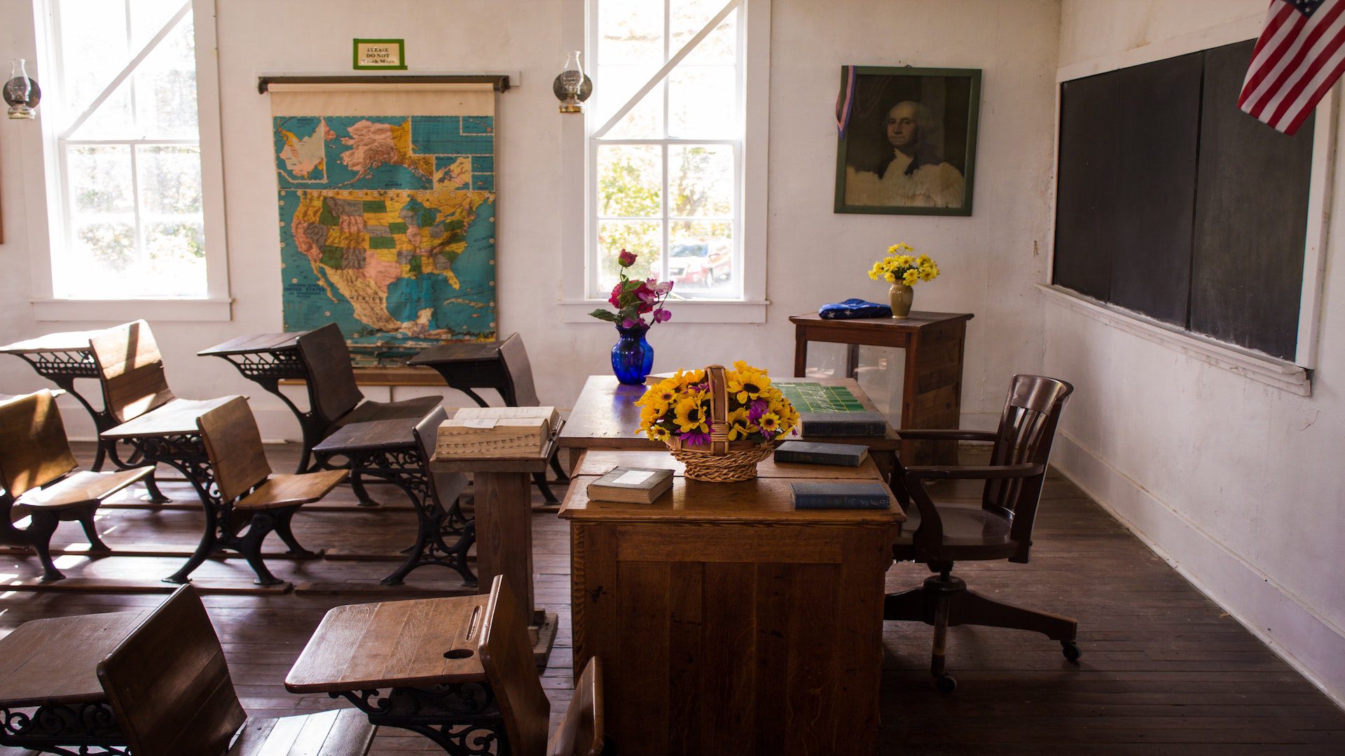 A school classroom with student desks, a teacher's desk at the front, and a chalkboard.