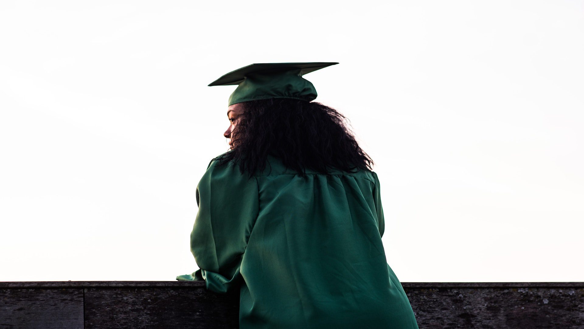 A woman in a cap and gown standing in front of a concrete wall.