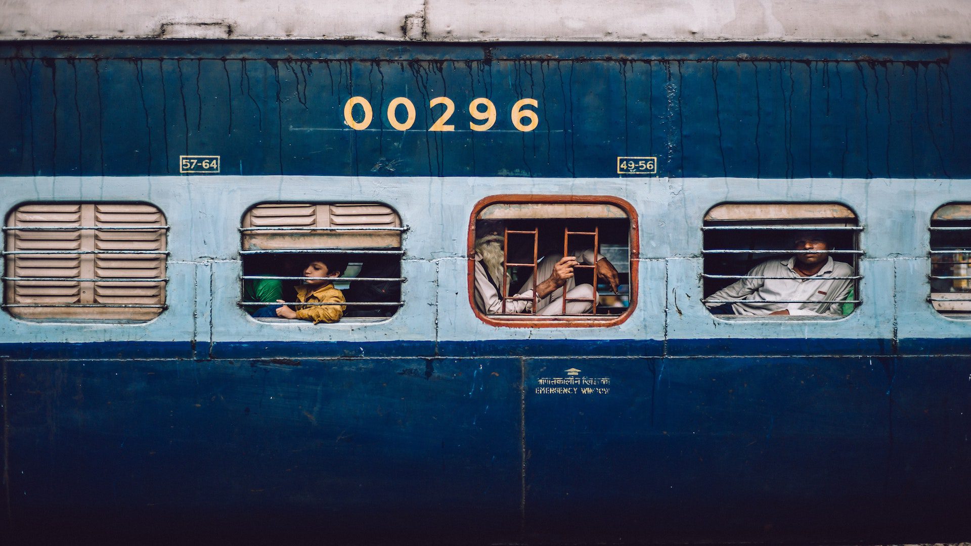 People looking through the windows of a blue train in India.