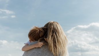 A mom holding her toddler son outside.