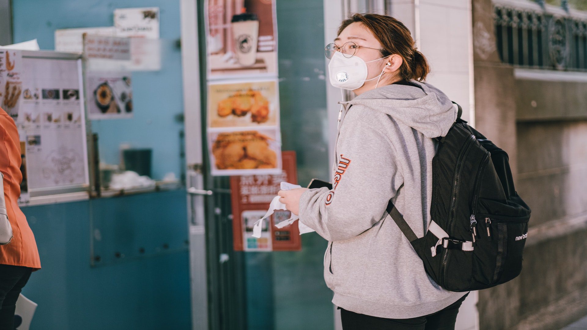 Woman in face mask waiting in a line to get food at a store.