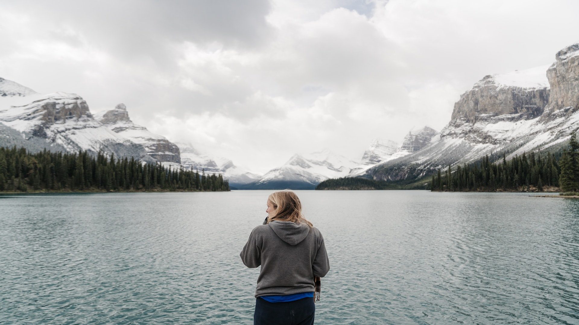 Woman standing in front of a lake and mountains during the winter.