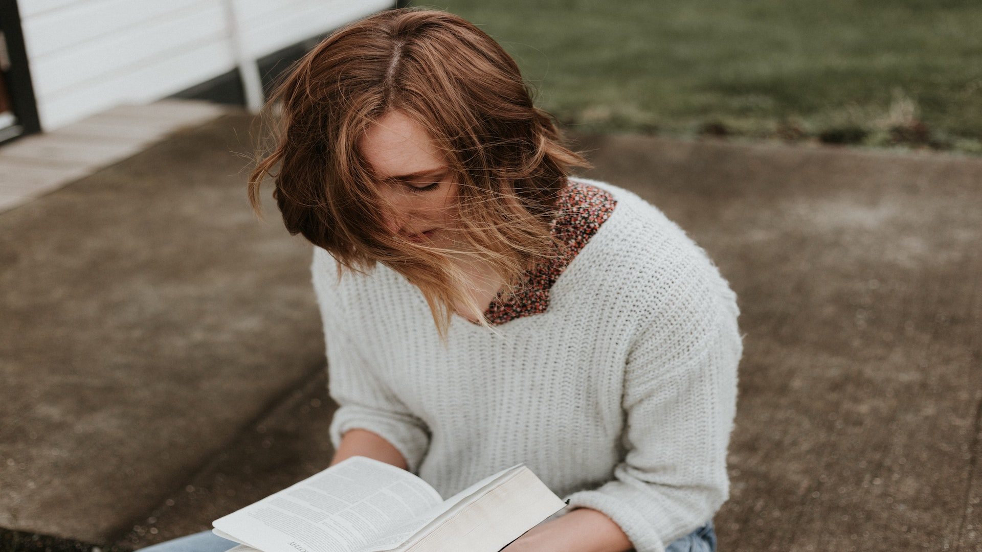 A woman reading a Bible while sitting down outside.