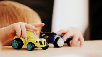 Toddler playing with toy cars on table.