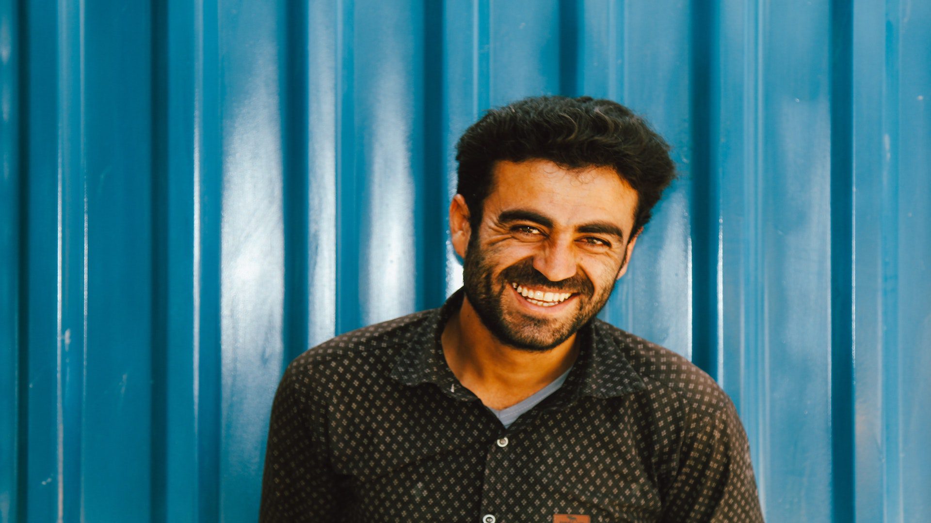 A middle aged man smiling in front of a blue wall.