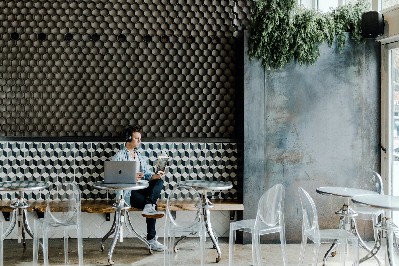 Man at coffee shop sitting at a table with a laptop and headphones.