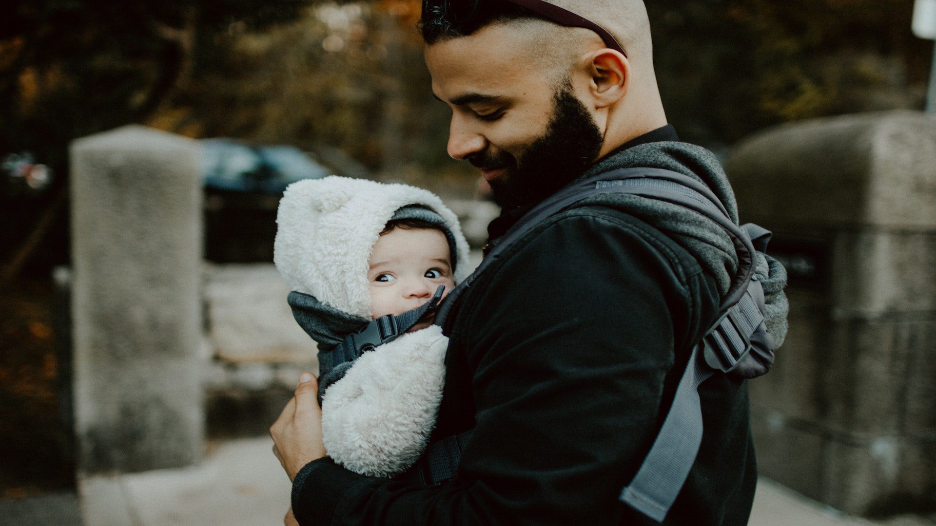 A dad holding a baby in a coat a baby carrier outside.