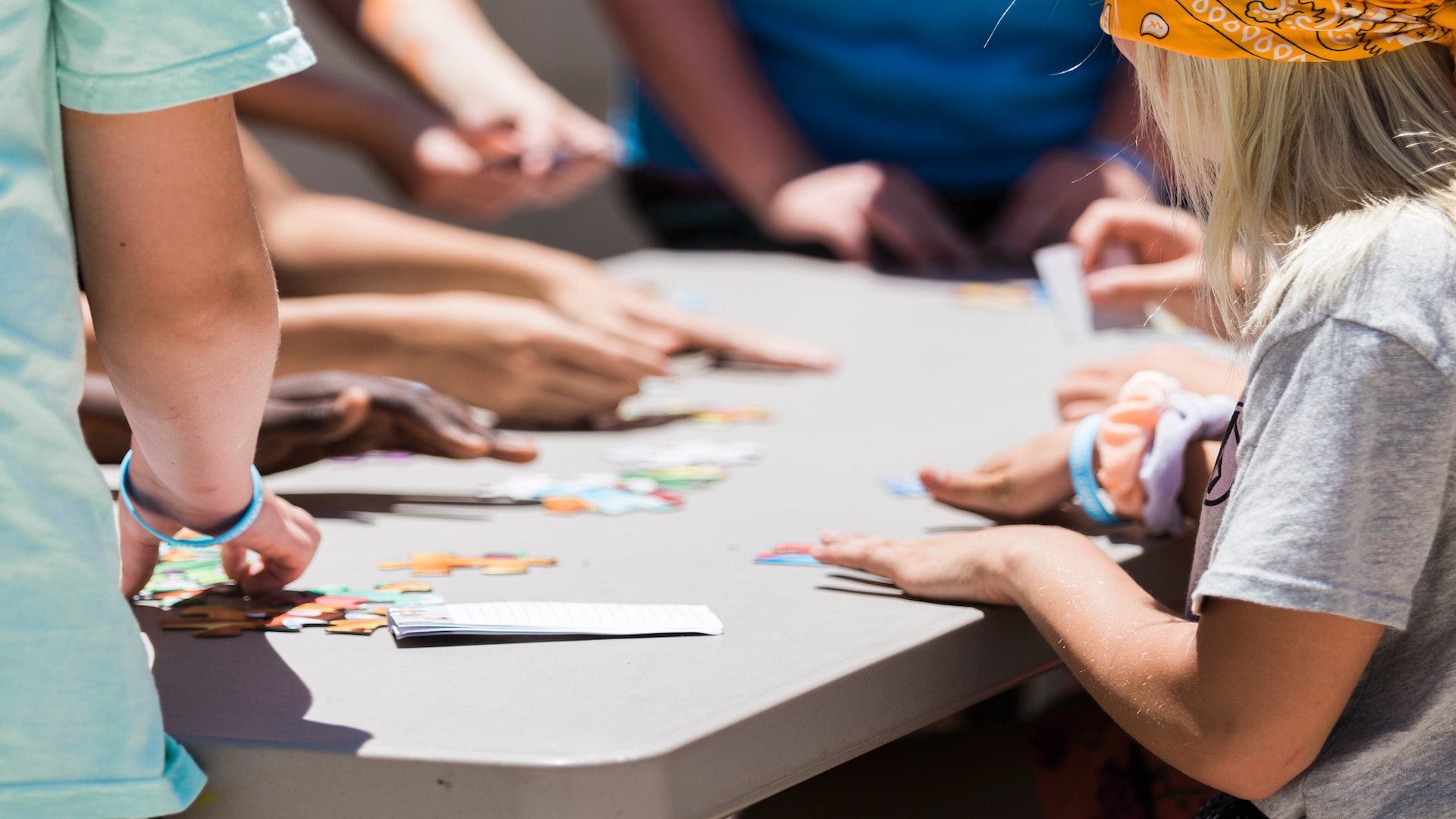 A group of kids sitting at a table outside playing a card game.