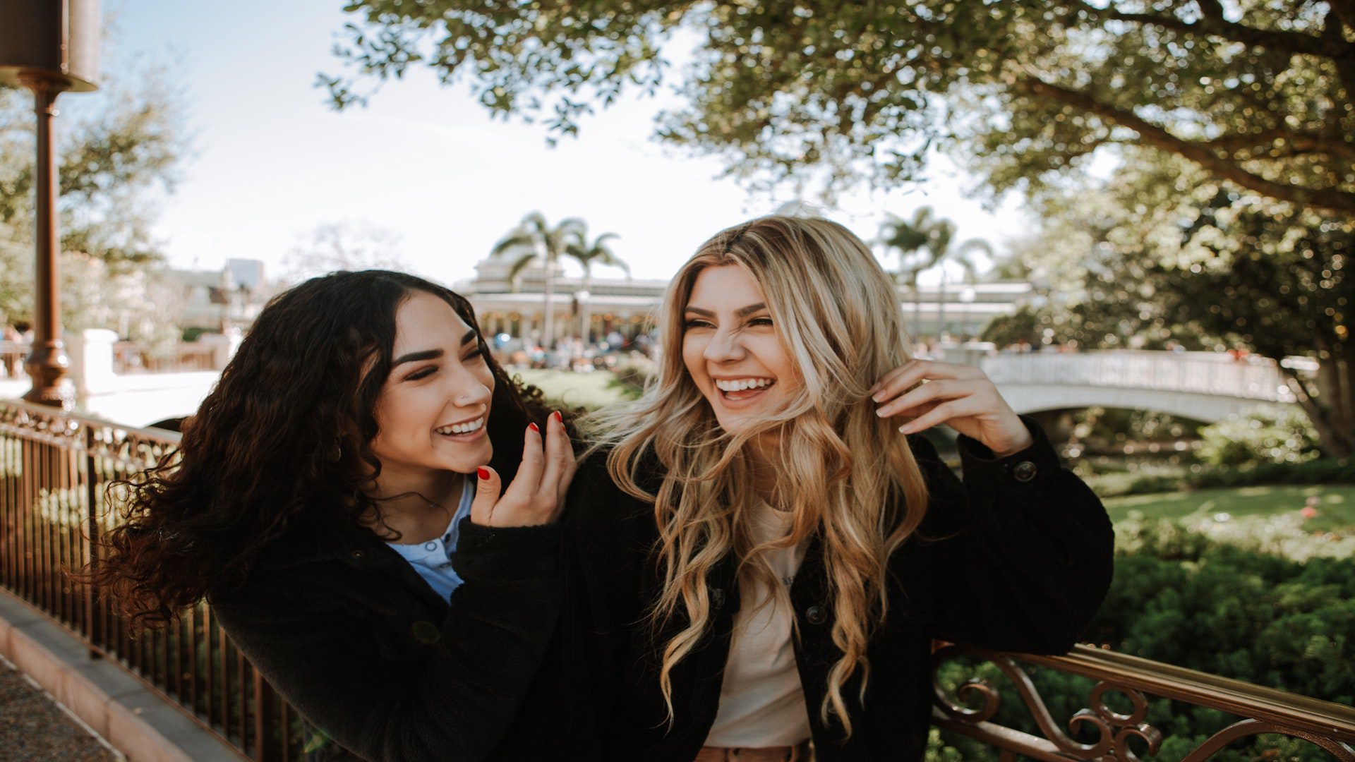 A girl with brown hair and a girl with blonde hair laughing outside.