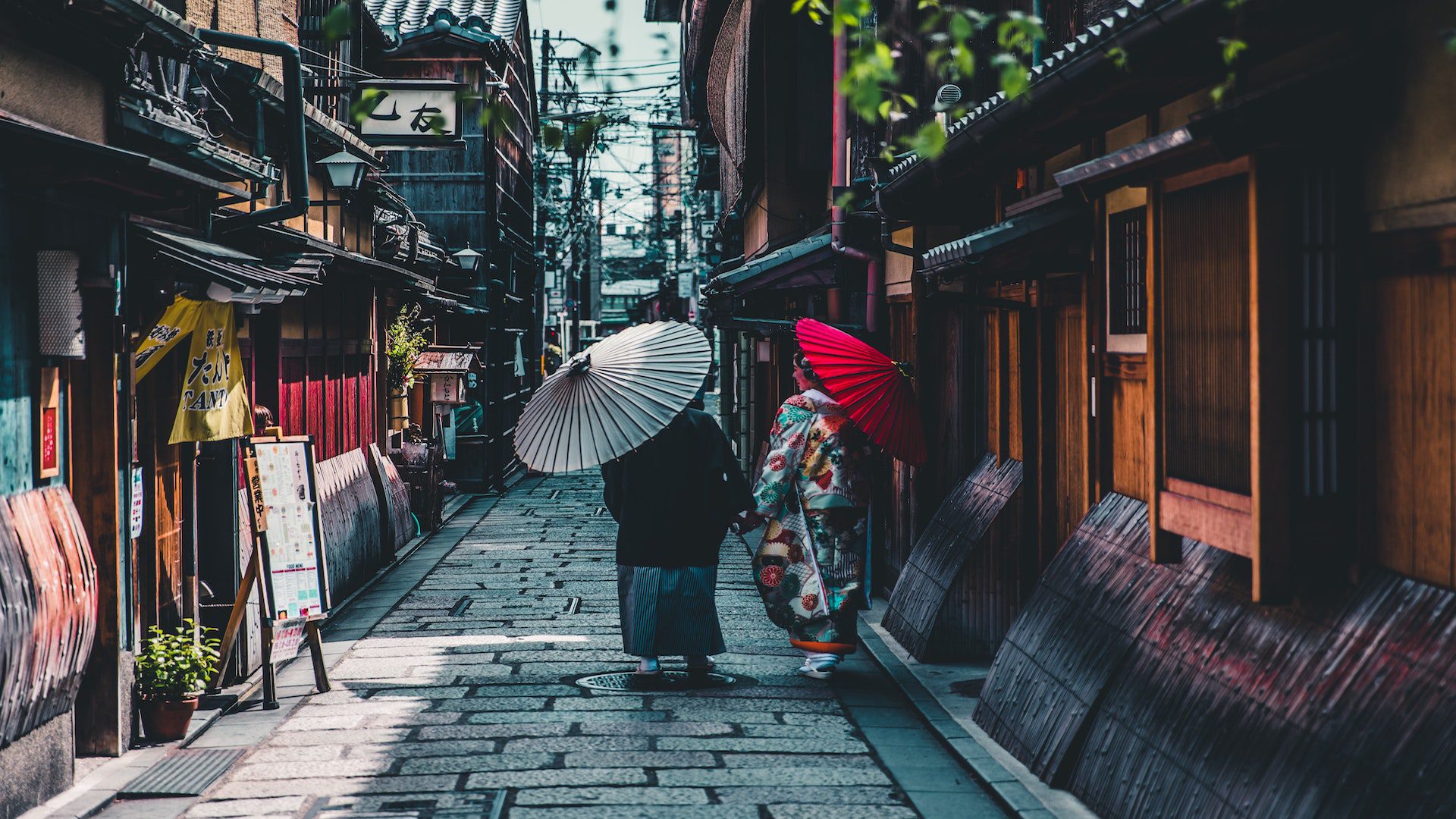 Two women with umbrellas walking down a brick street in Japan.