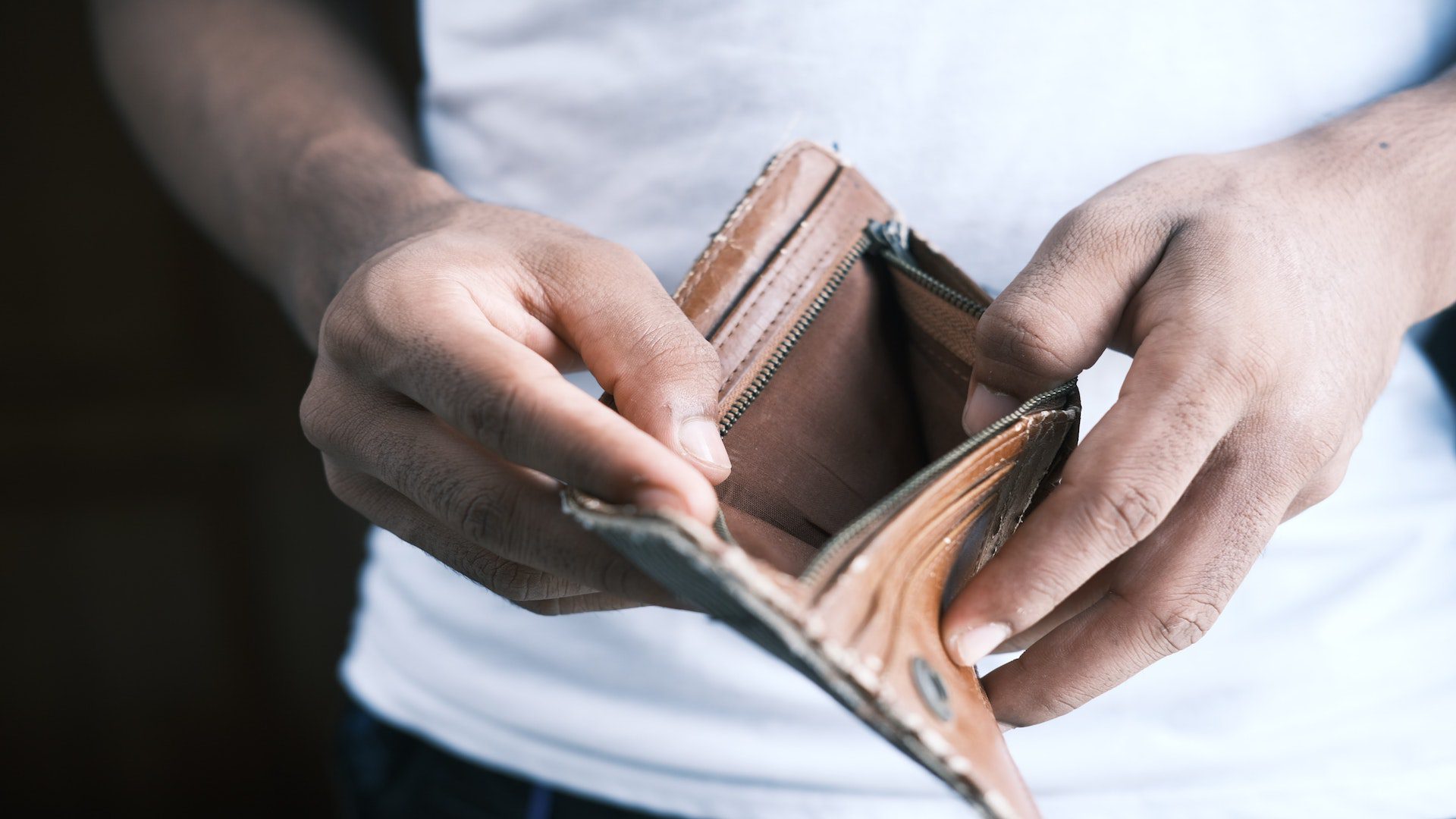 A man in a white shirt holding an open, empty leather wallet.