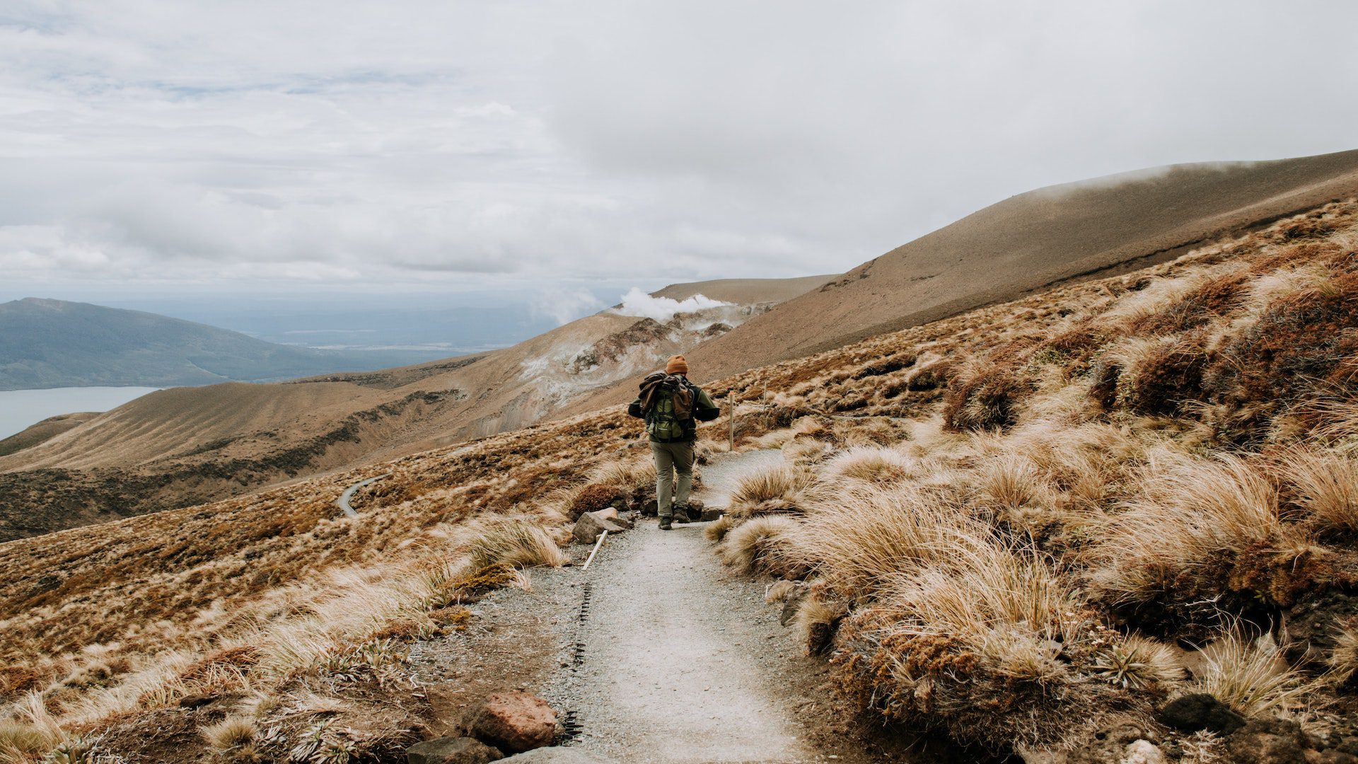 A man walking on a path on a mountain near a river.