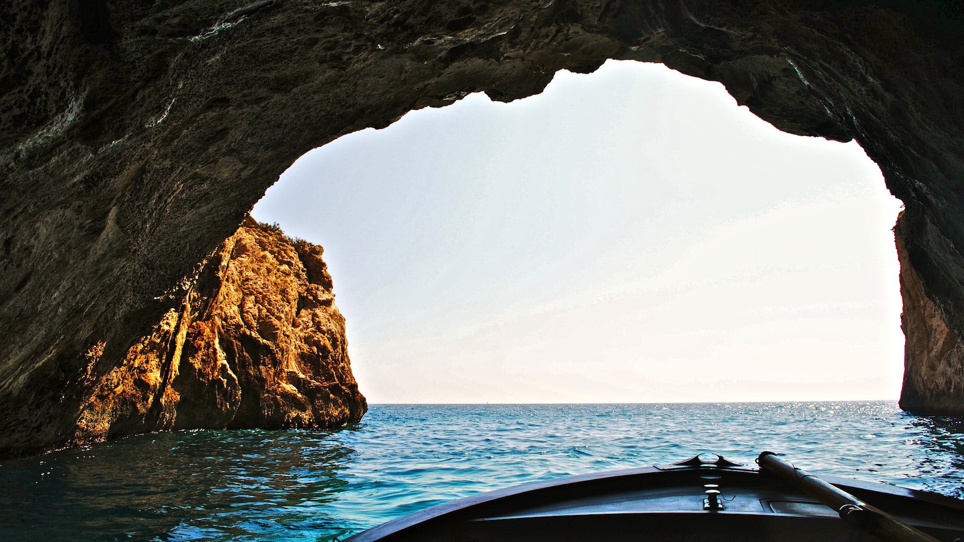 A boat inside of a water cave, looking out toward the open ocean.