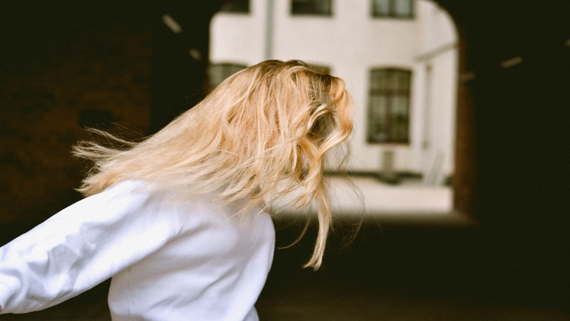 A woman on a street in a white sweatshirt with blonde hair covering her face.