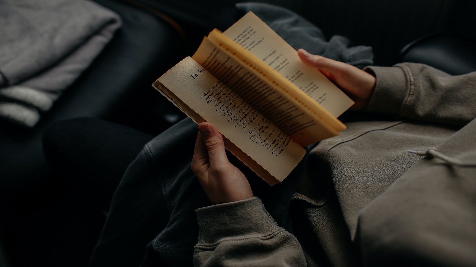 A person in a green sweatshirt sitting and reading a book.