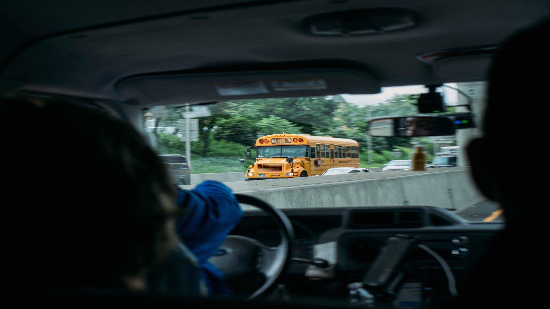 A person driving a car with a school bus passing on the other side of the street.