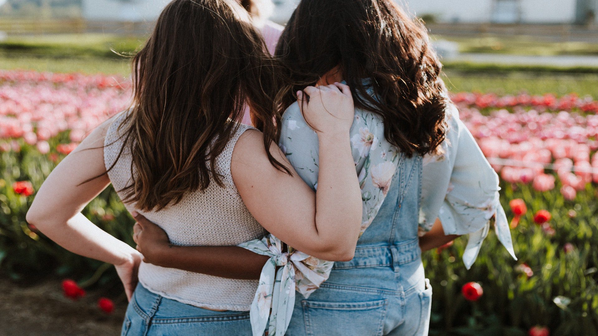 A white woman and an African American woman hugging in a flower field.