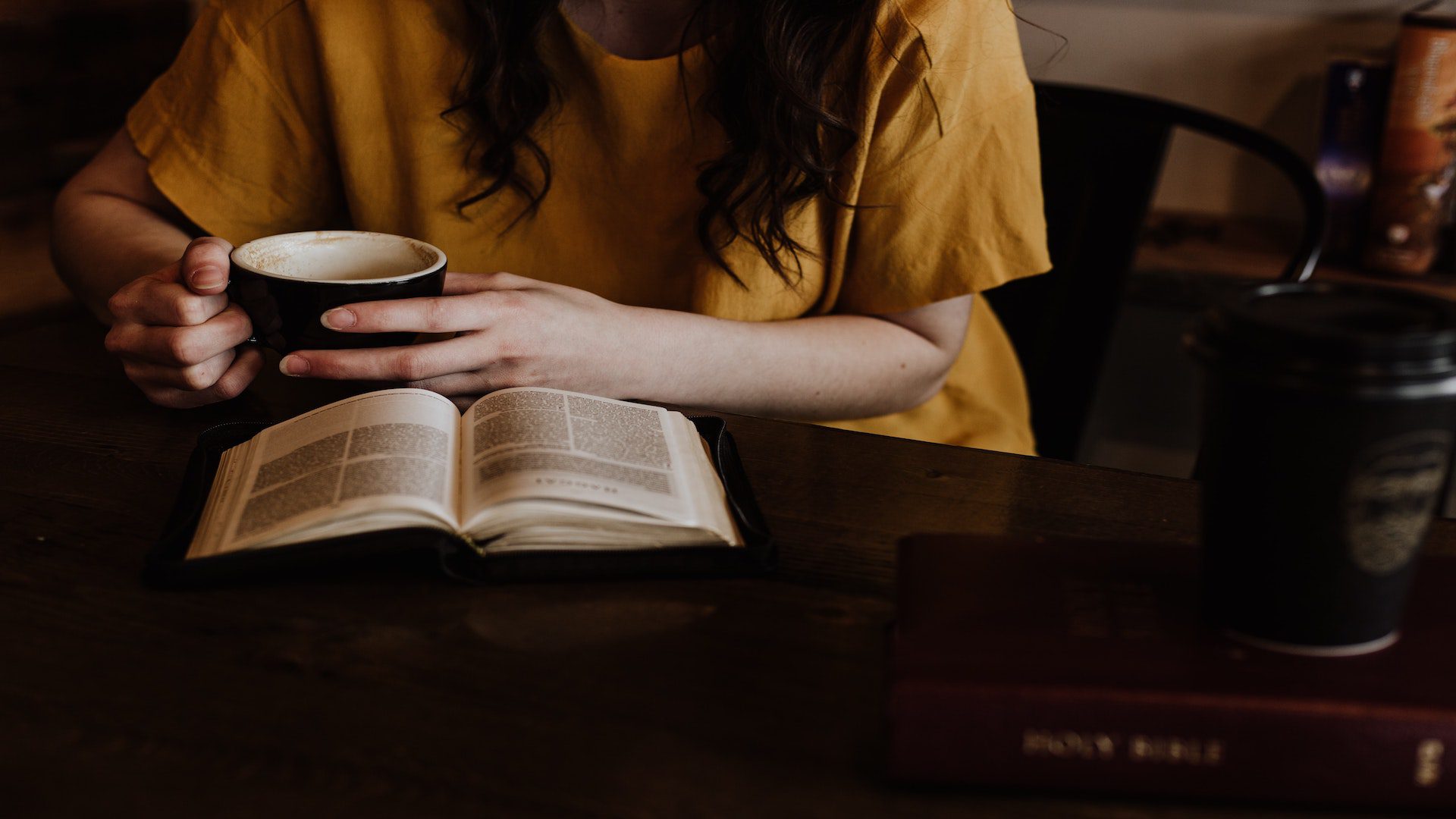 A woman sitting at a table with a coffee and book.