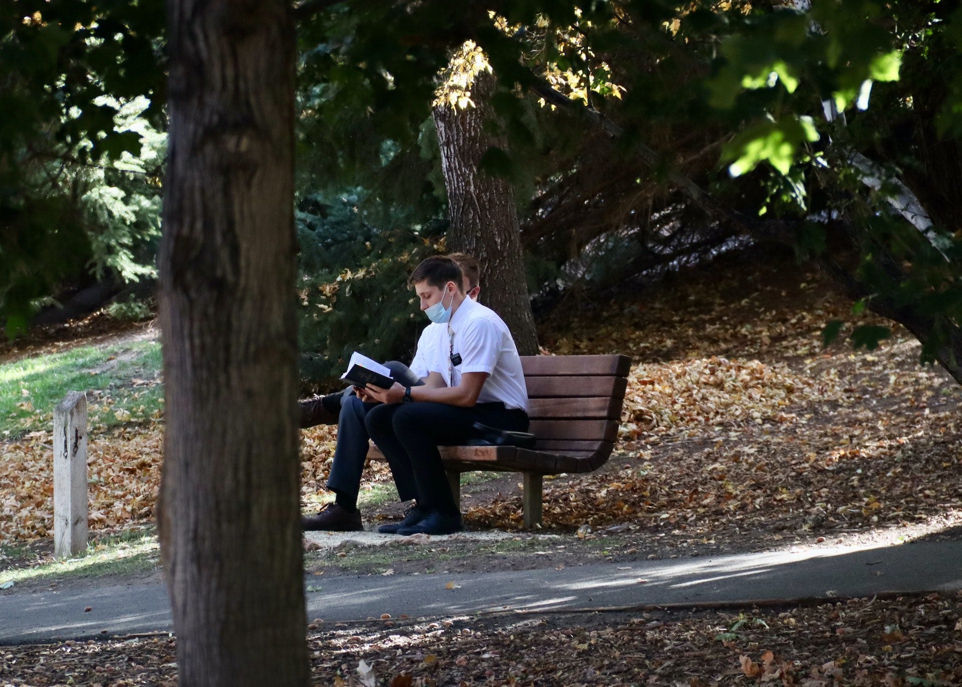 Mormon missionaries sit on a bench in an empty park.