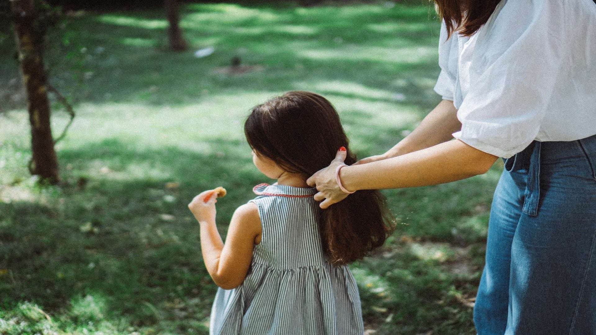 A mom putting her daughter's hair into a ponytail outside.