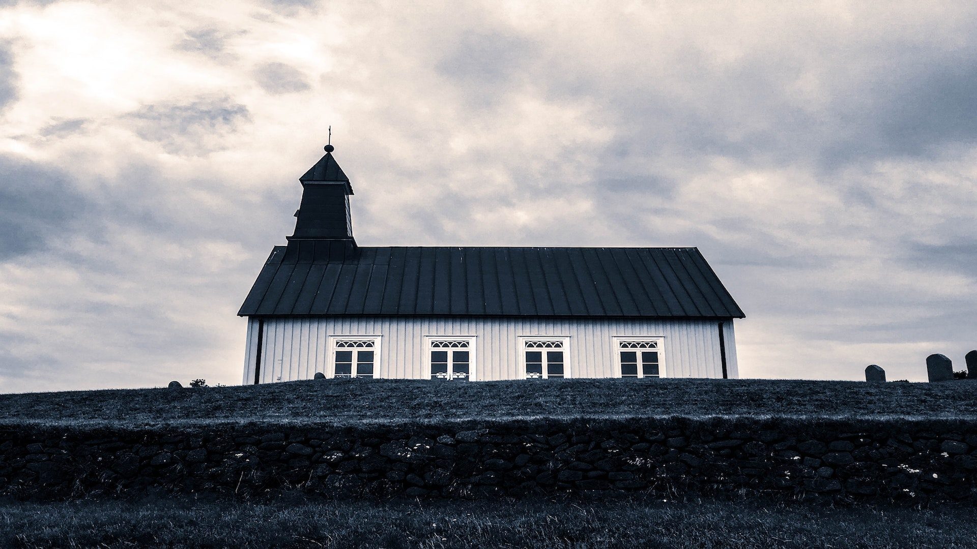 Looking up a hill at a white church with a black roof and steeple.