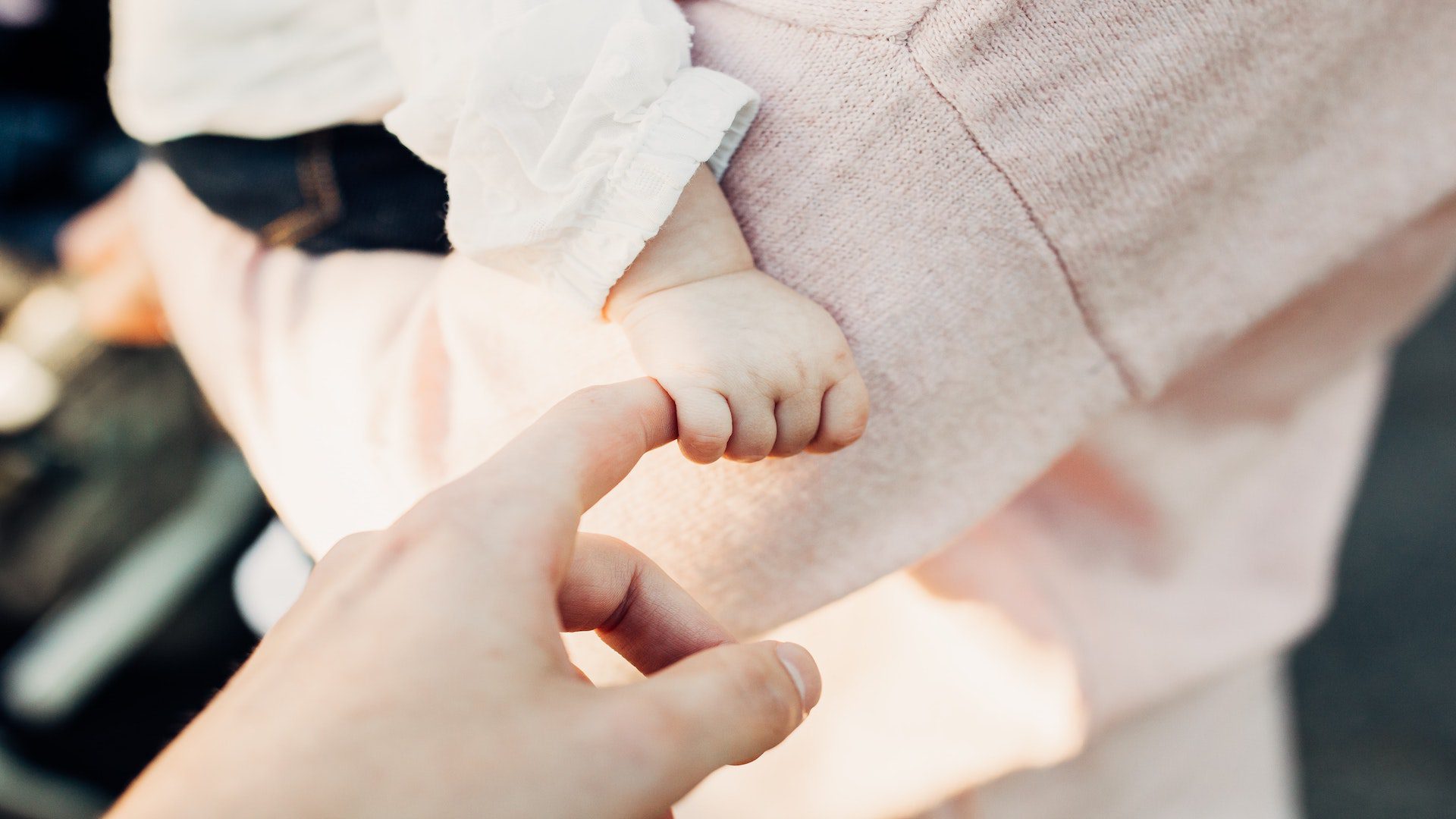 Mom in pink sweater holding baby who is holding the dad's hand.