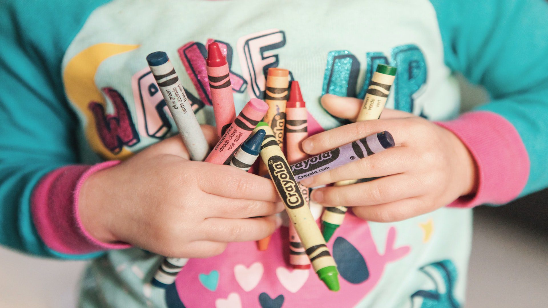 A young girl in pajamas holding crayons of different colors.