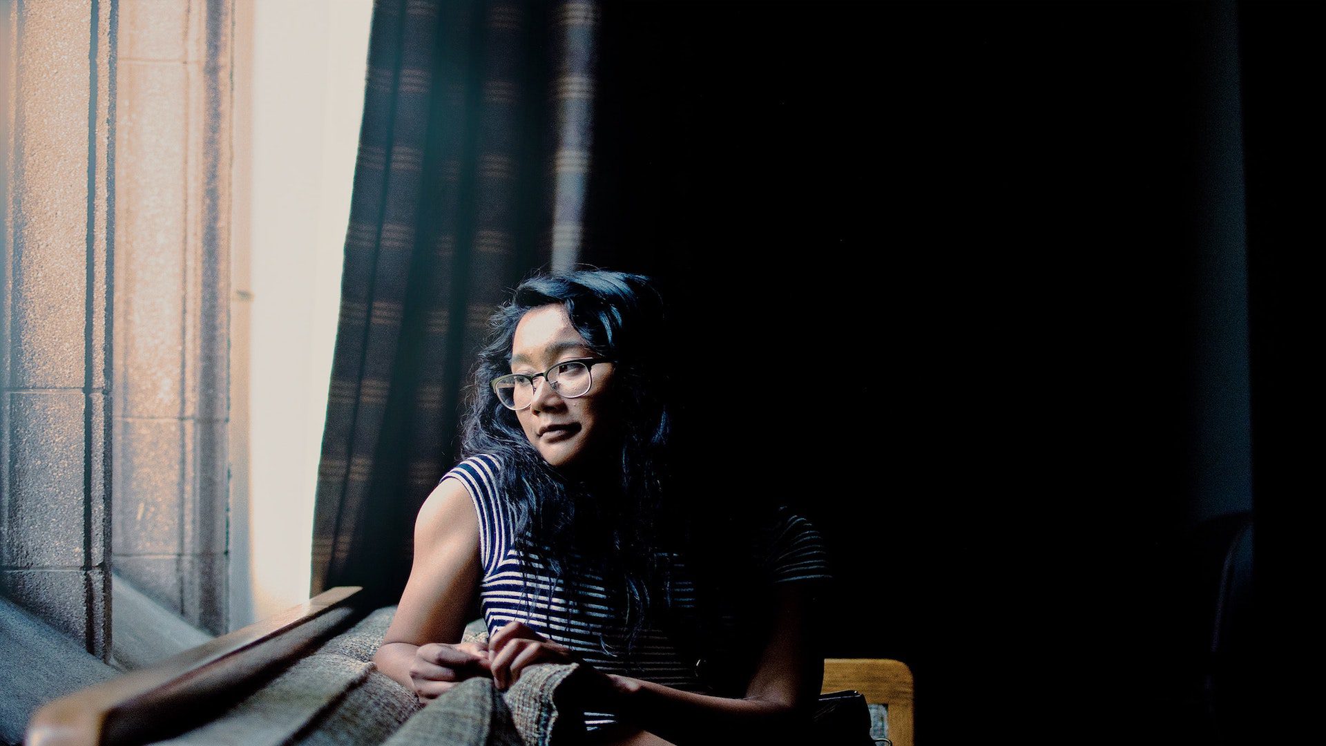 A woman sitting on a bench looking outside a window.