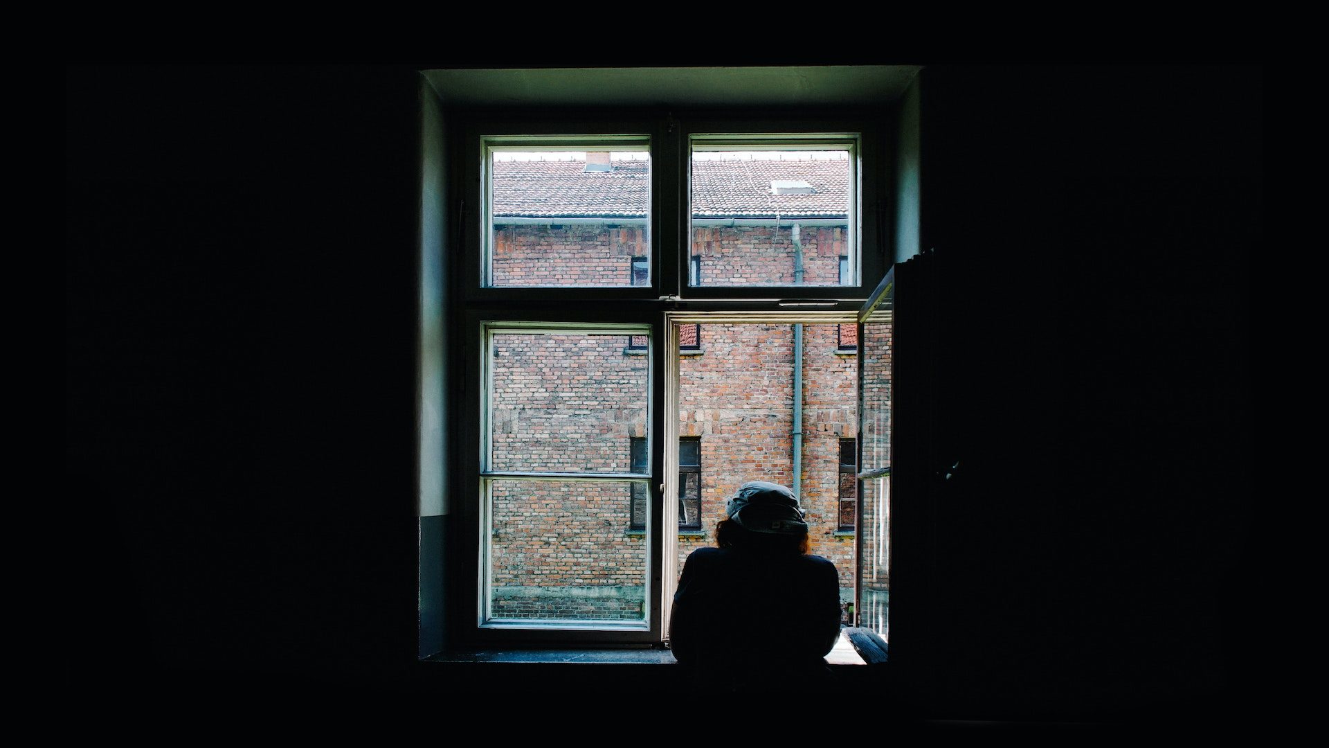 Person looking out a window at a brick building.