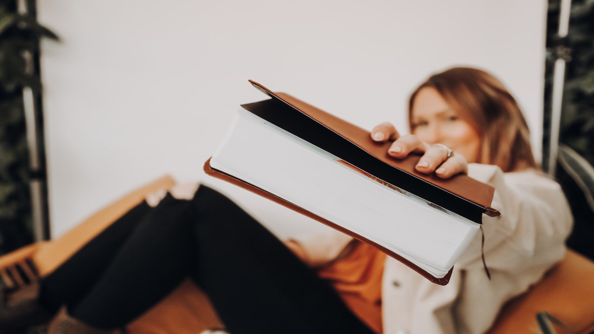 Woman in black pants and tan shirt sitting and holding out her Bible.