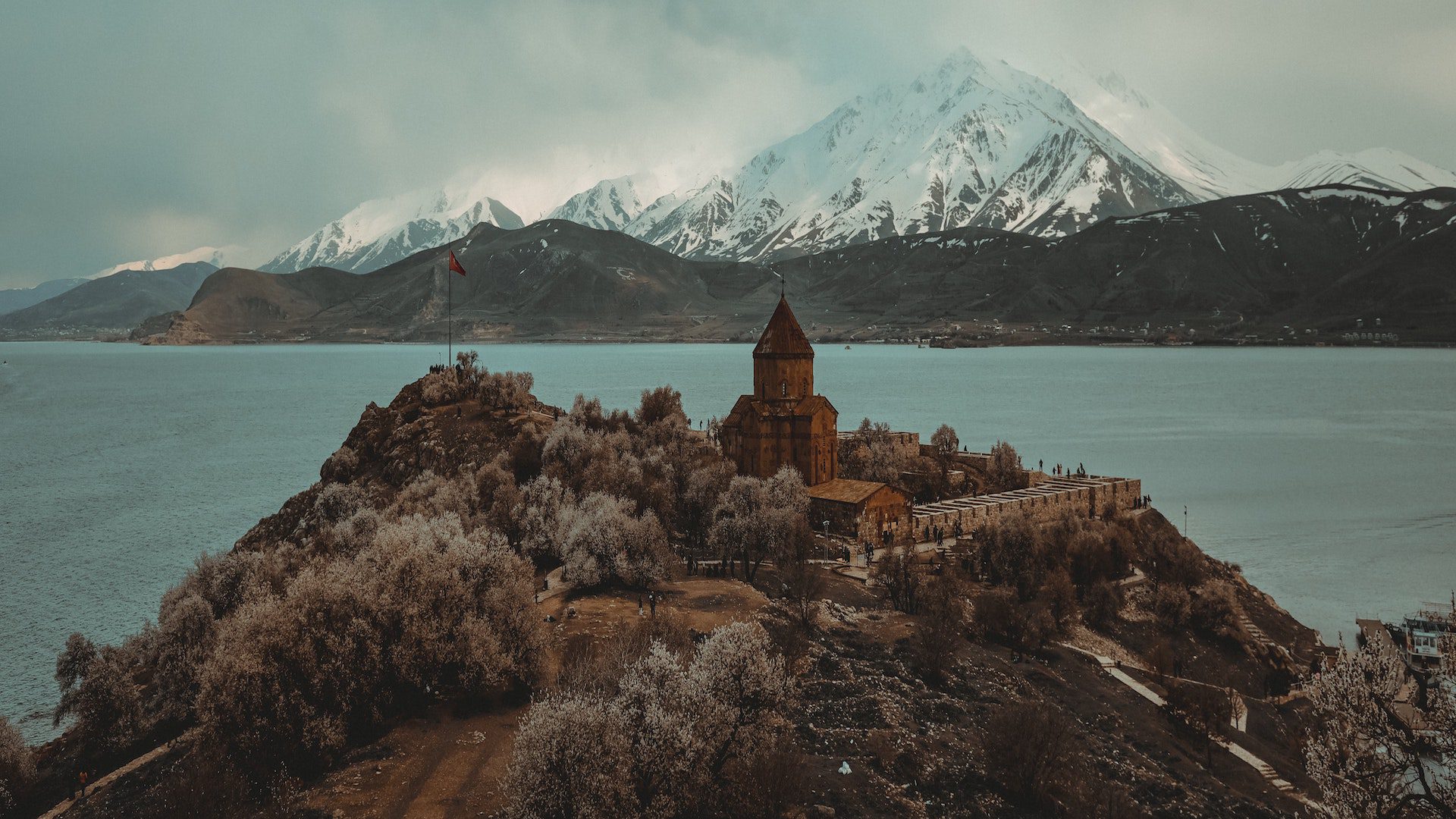 A church on a hill that is surrounded by a body of water on an overcast day.