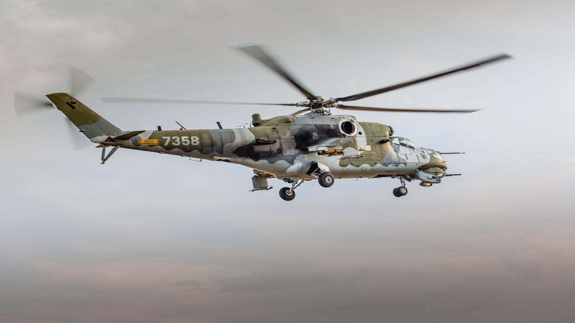 Military helicopter with gray and green camo flying in the air.
