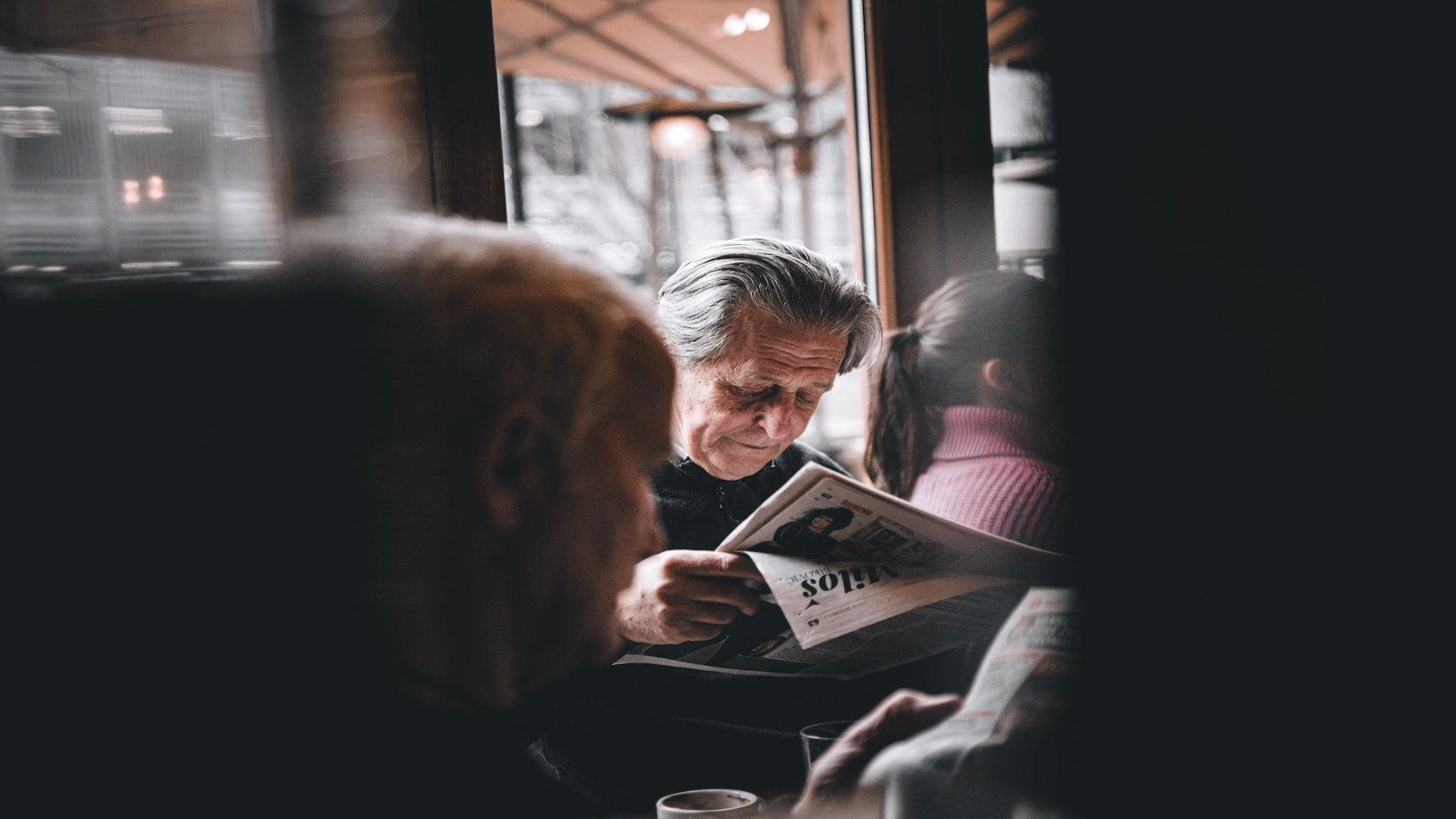 An elderly man reading a newspaper in a cafe.