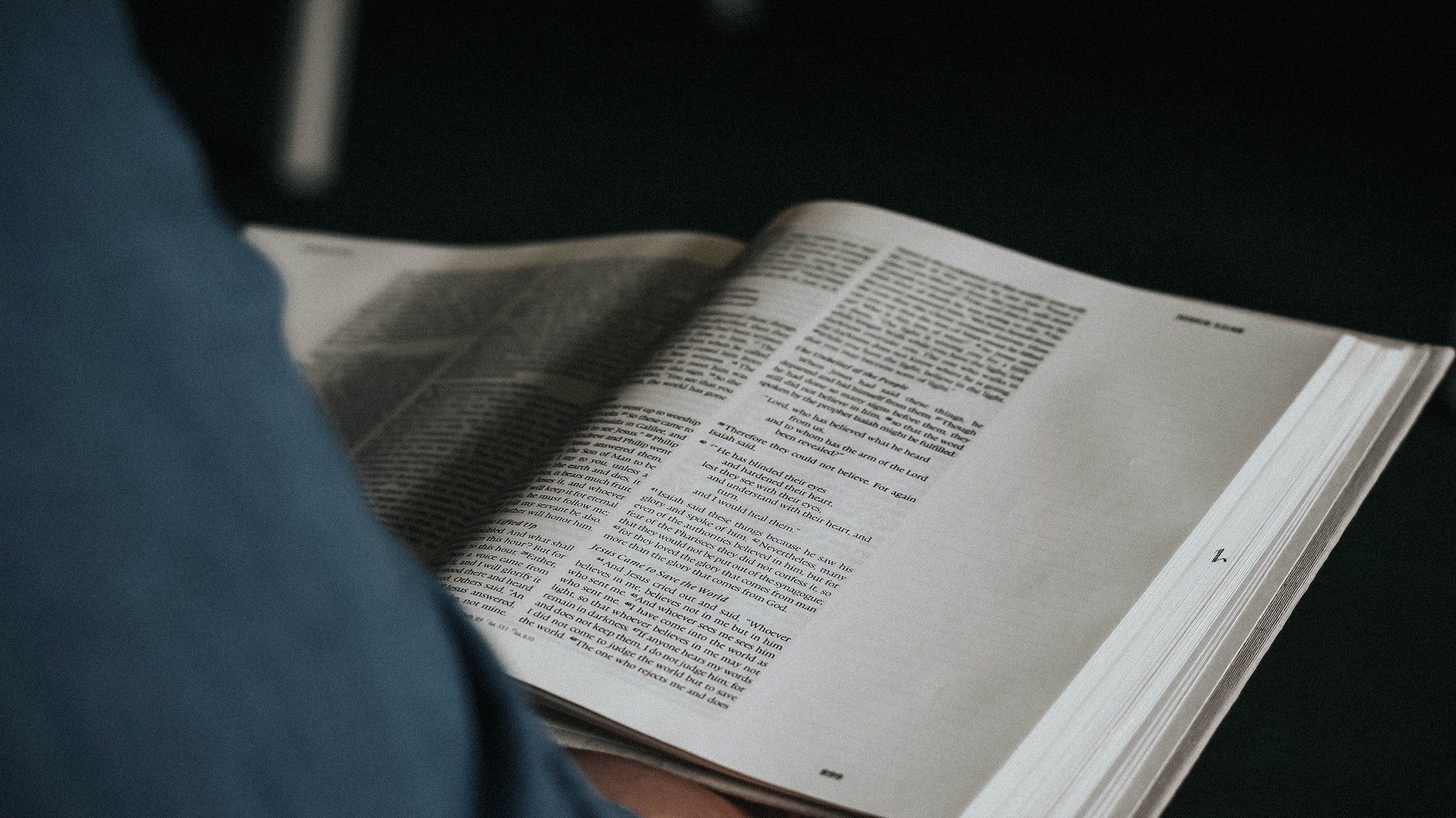 A person in a blue shirt holding an open Bible.
