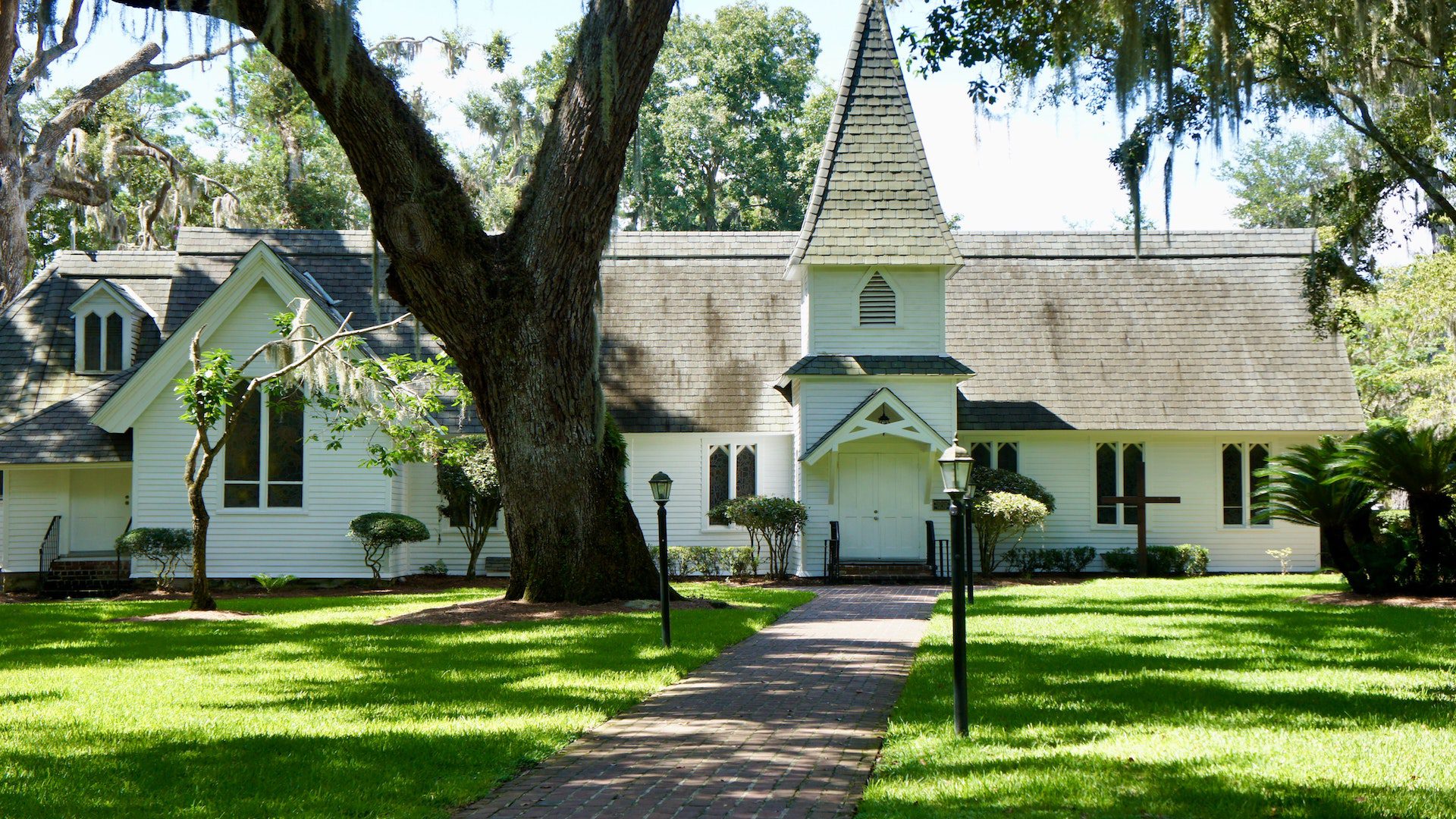 White church with a black roof with green grass and a sidewalk.